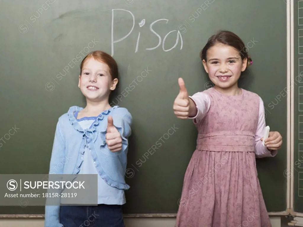 Girls standing in front of blackboard, thumbs up