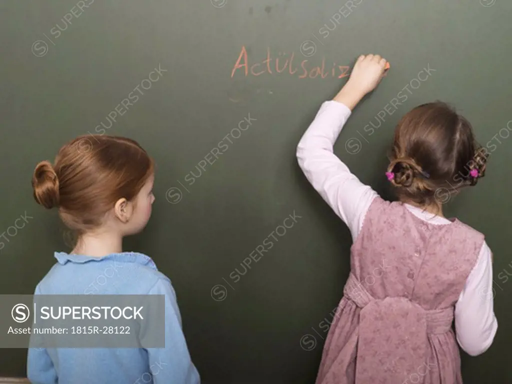 Girls standing in front of blackboard, writing, rear view
