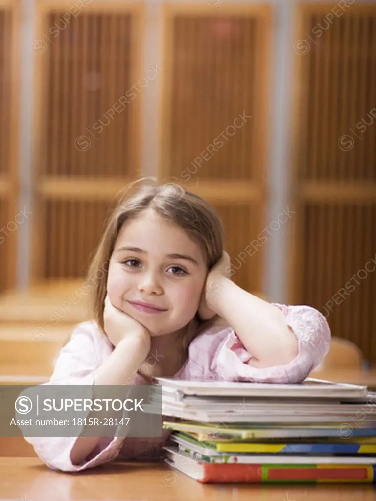 Girl sitting at school desk, leaning on stack of books