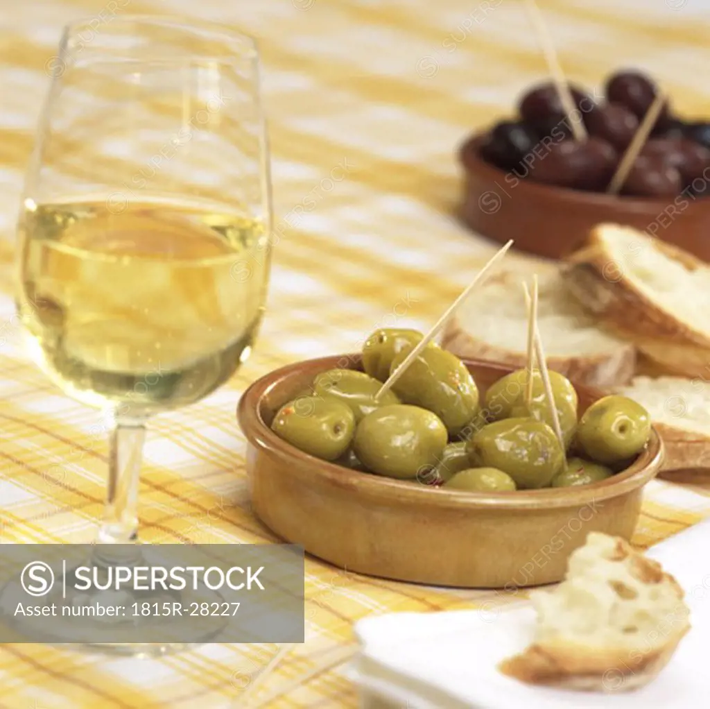 Glass of wine with olives and white bread on table
