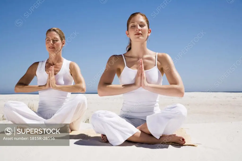 Two women exercising yoga on beach