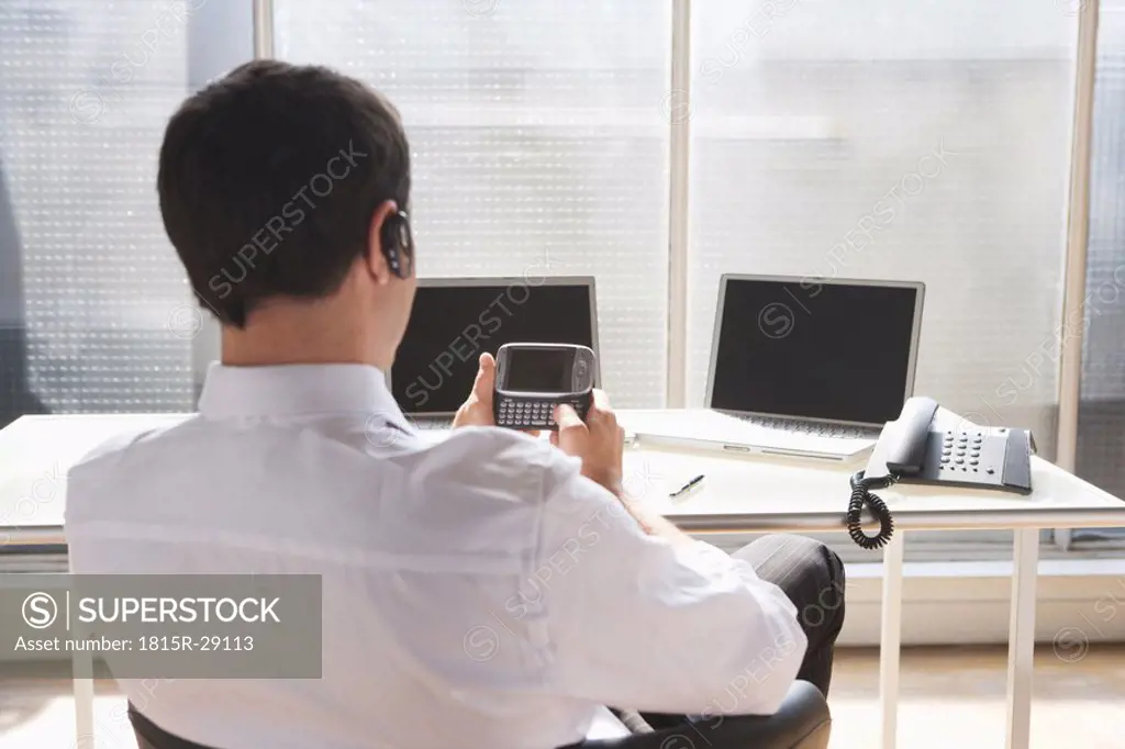 Business man using headset and mobile phone, rear view