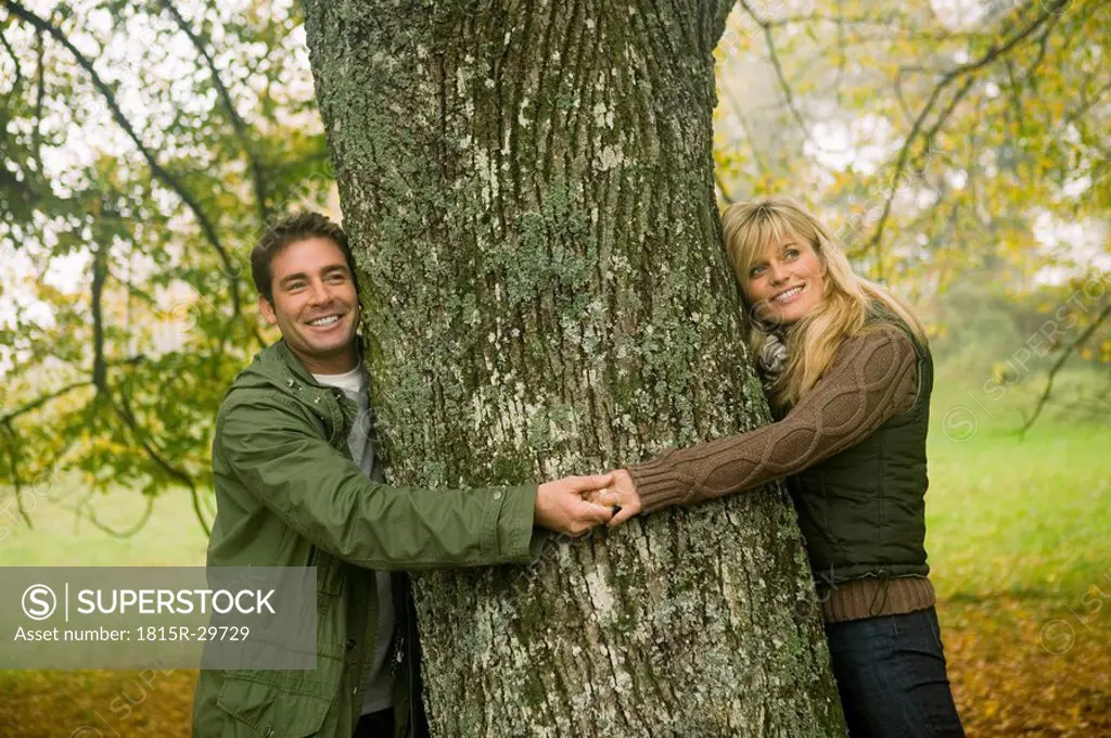 Germany, Baden-Württemberg, Swabian mountains, Couple smiling and hugging tree, portrait