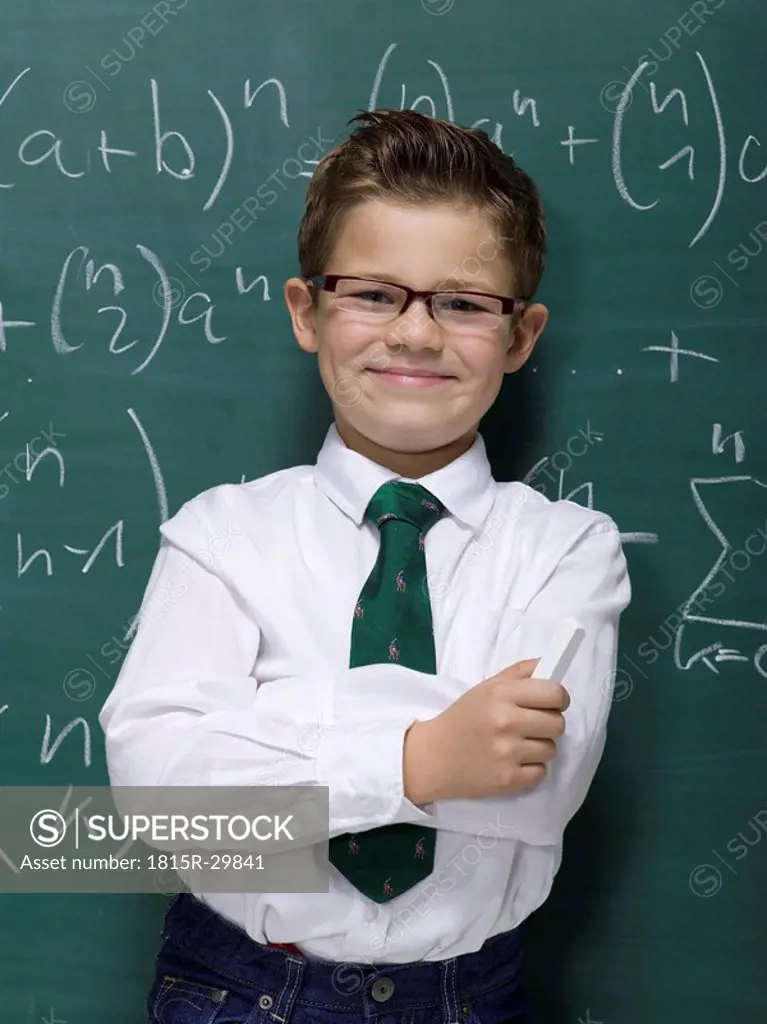 Boy 10-11 leaning against blackboard, smiling, portrait, close-up