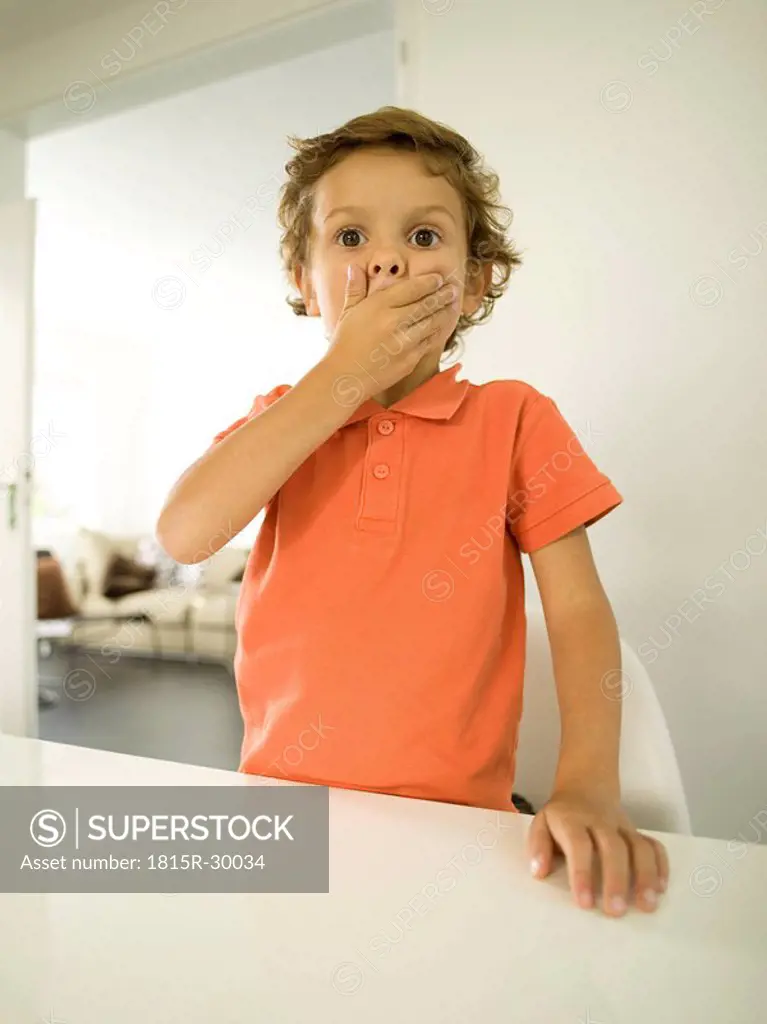 Young boy 4-5 covering his mouth with his hands, portrait