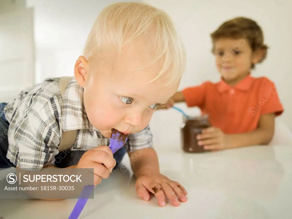 Two boys 4-5, 12-24 months, boy licking chocolate from spoon, portrait