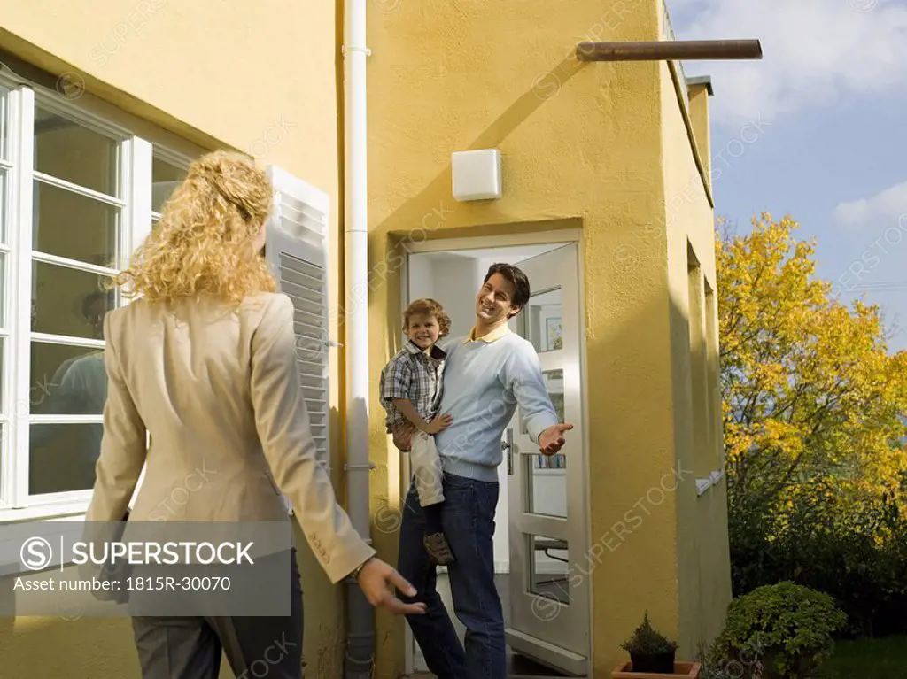 Father at door holding boy 3-4, mother coming home