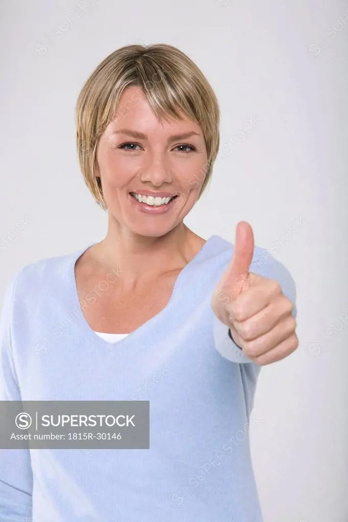 Young woman making thumbs up gesture, smiling, portrait
