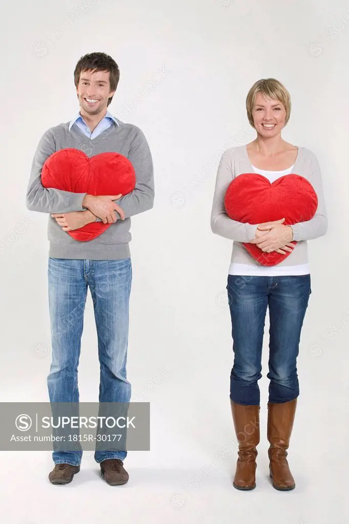 Young couple holding heart-shaped cushion, portrait