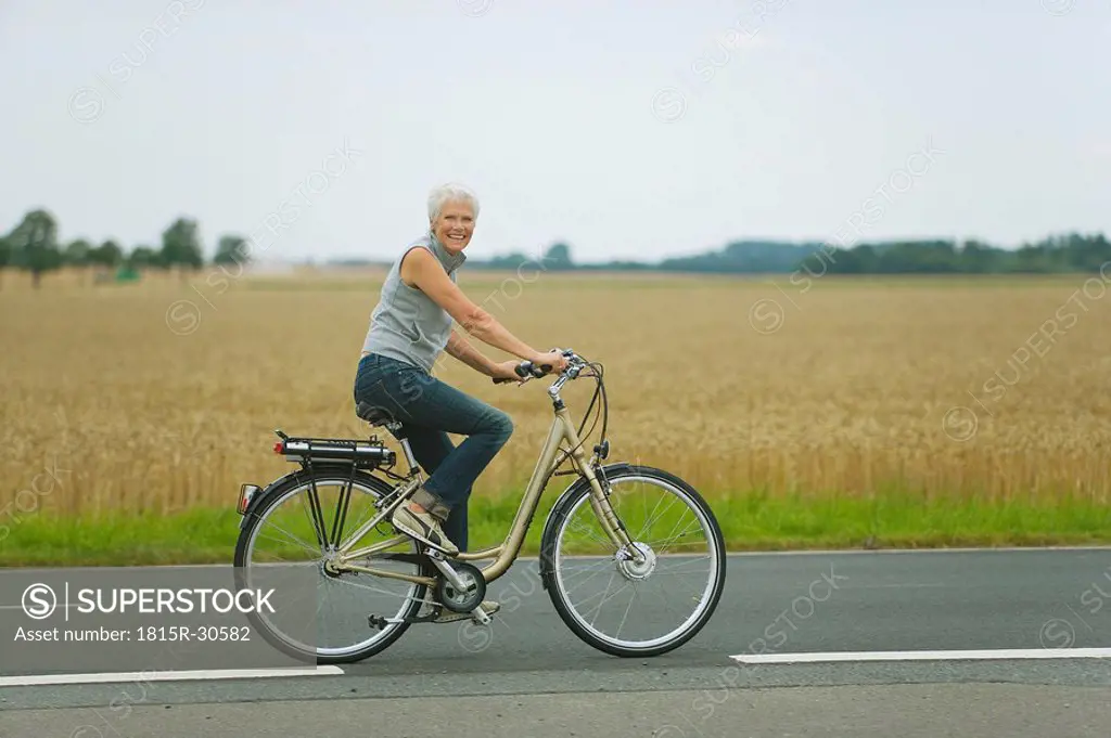 Senior woman biking on road