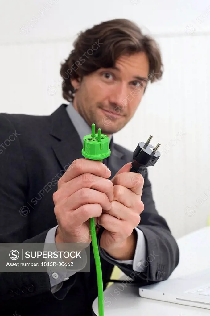 Businessman holding green and black plugs