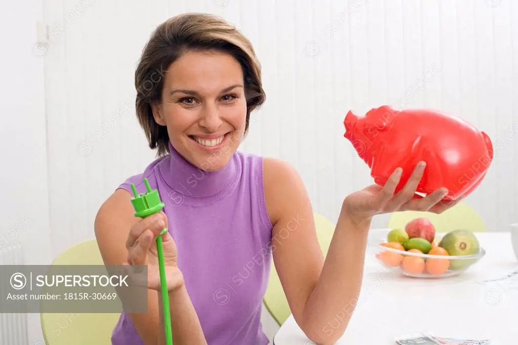 Woman holding green plug and piggy bank