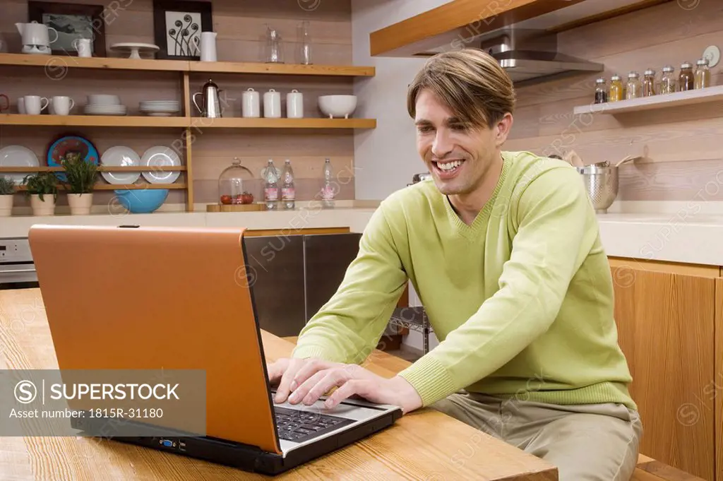 Young man sitting in kitchen using laptop, portrait