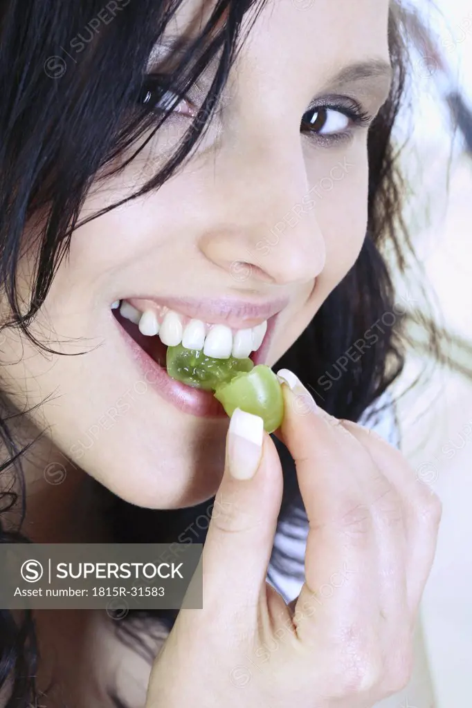 Young woman eating grape, close-up, portrait