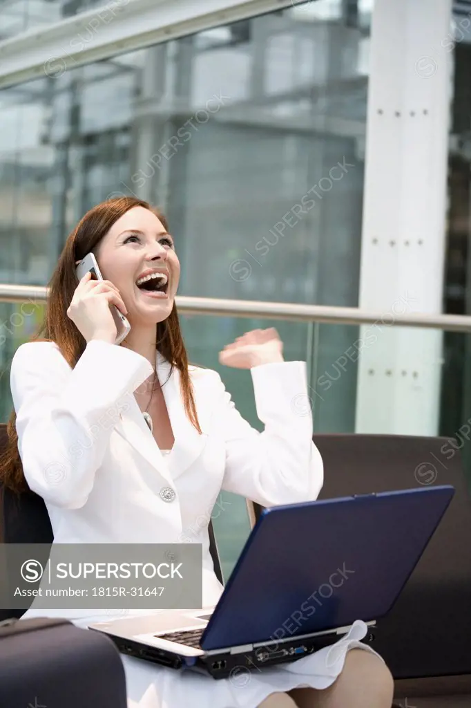 Business woman sitting in airport lounge with laptop, using mobile phone