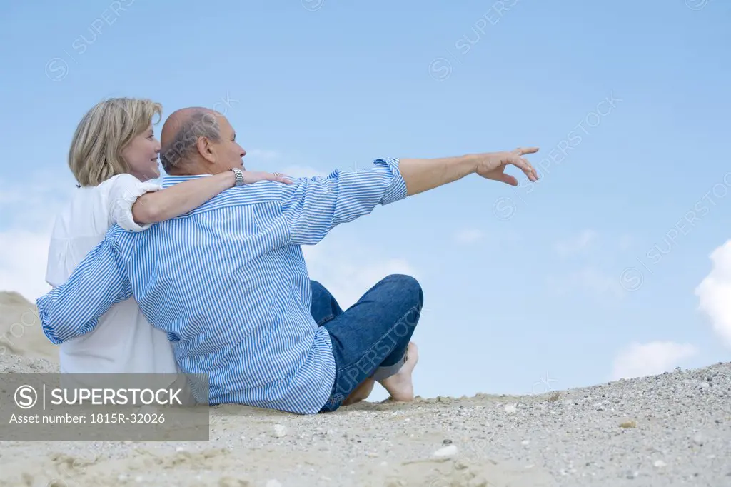 Mature couple sittiing on beach, man pointing