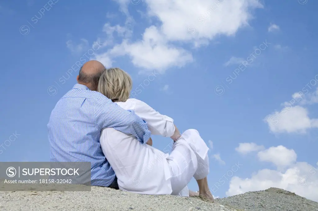 Mature couple sitting on beach, rear view