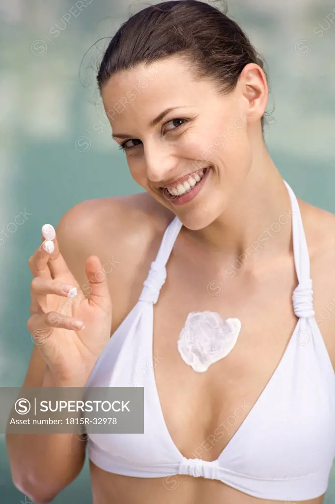 Young woman applying moisturizer to her body, smiling, portrait