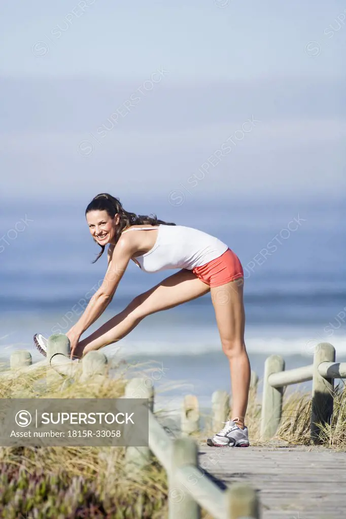 South Africa, Young woman stretching leg by fence