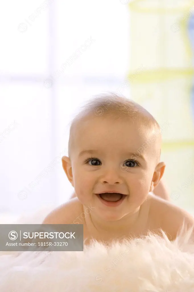 Baby boy ( 6-12 months) lying on belly, smiling, close-up