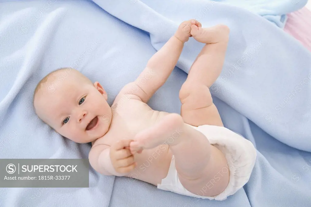 Baby boy (6-9 months) lying on bed, touching toes