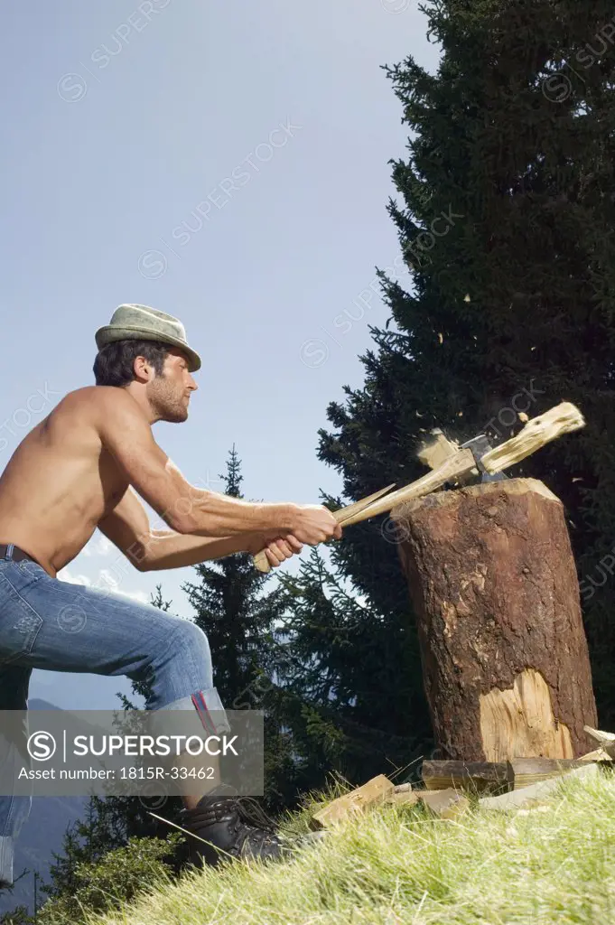 Young man chopping wood, side view