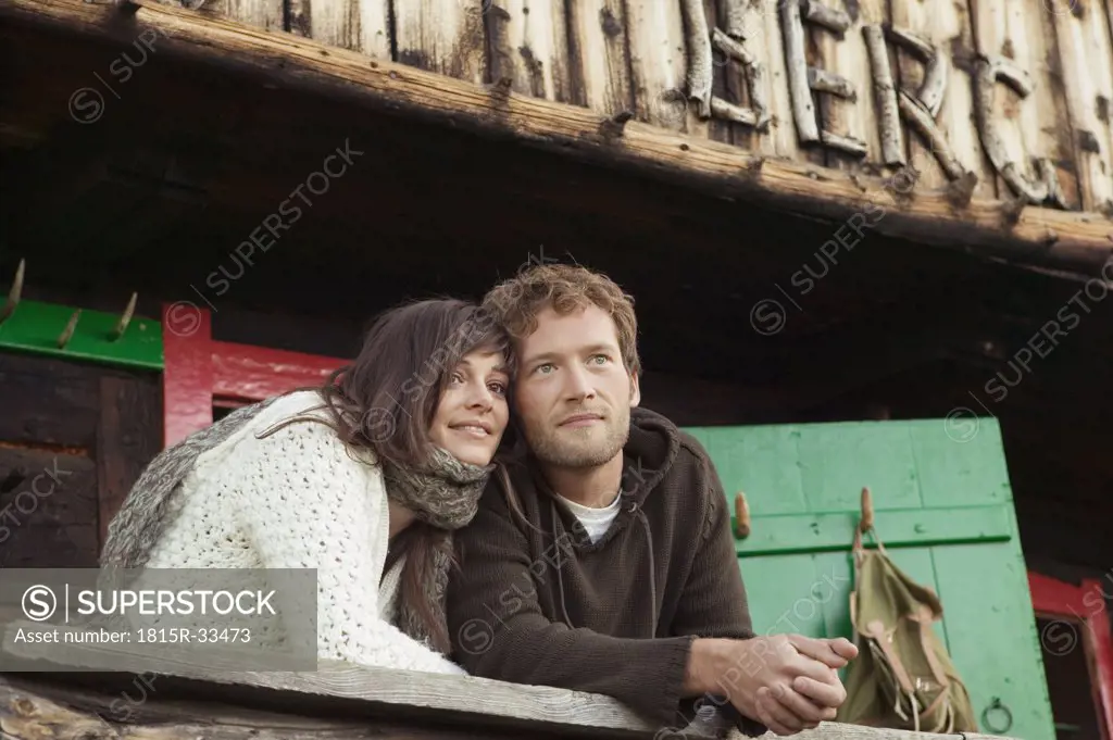 Young couple leaning on wooden rail in front of alpine hut