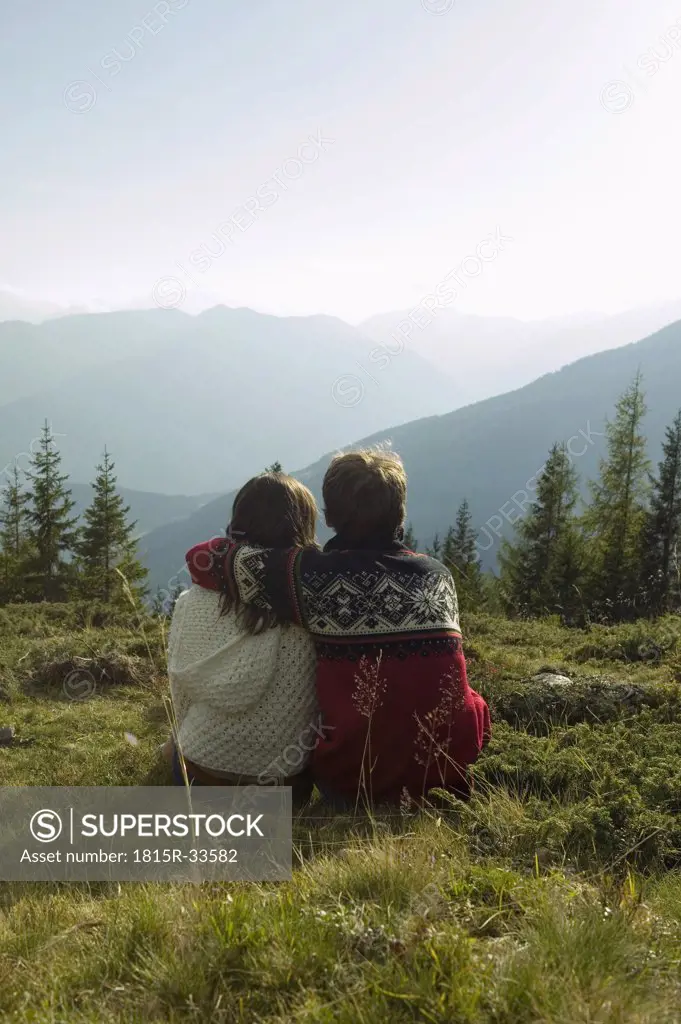 Young couple sitting in meadow in mountains, rear view