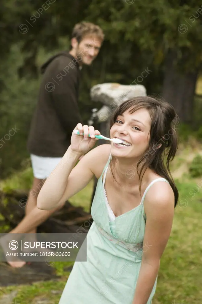 Young couple, woman brushing teeth, man standing in background