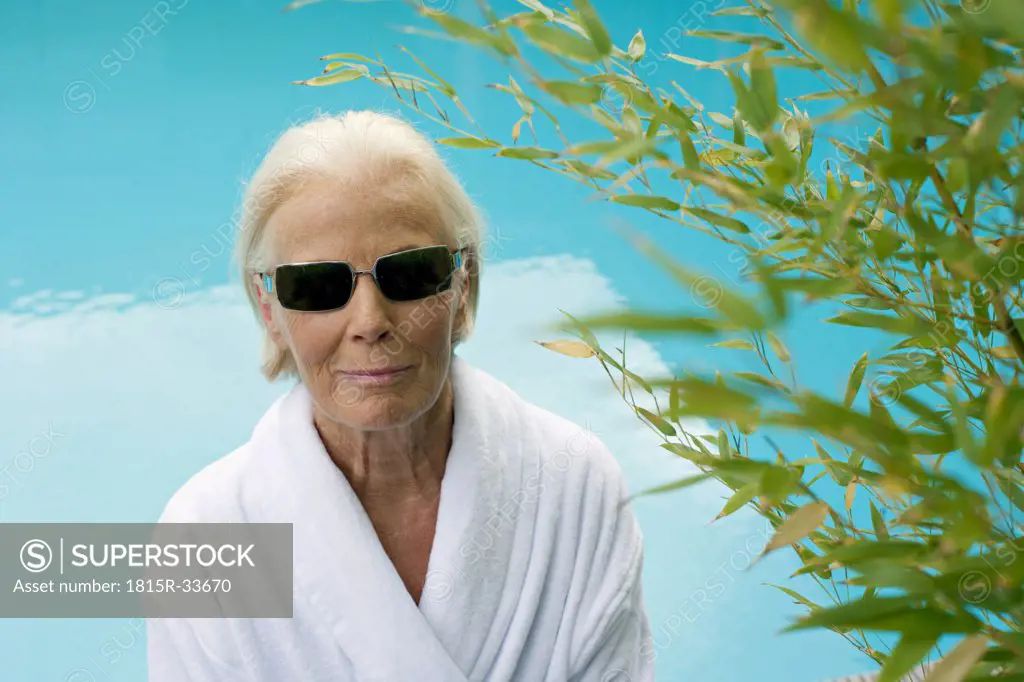 Germany, senior woman at pool, wearing sun glasses