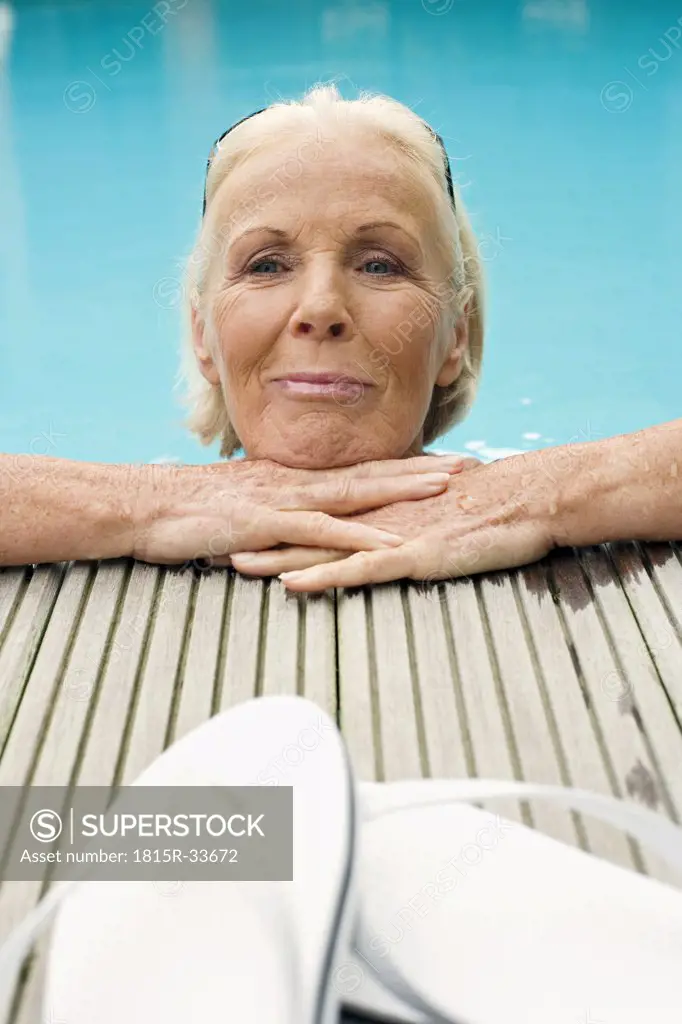 Germany, Senior woman resting on edge of pool, smiling