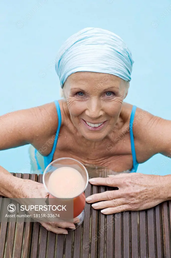 Germany, senior woman having cocktail at pool