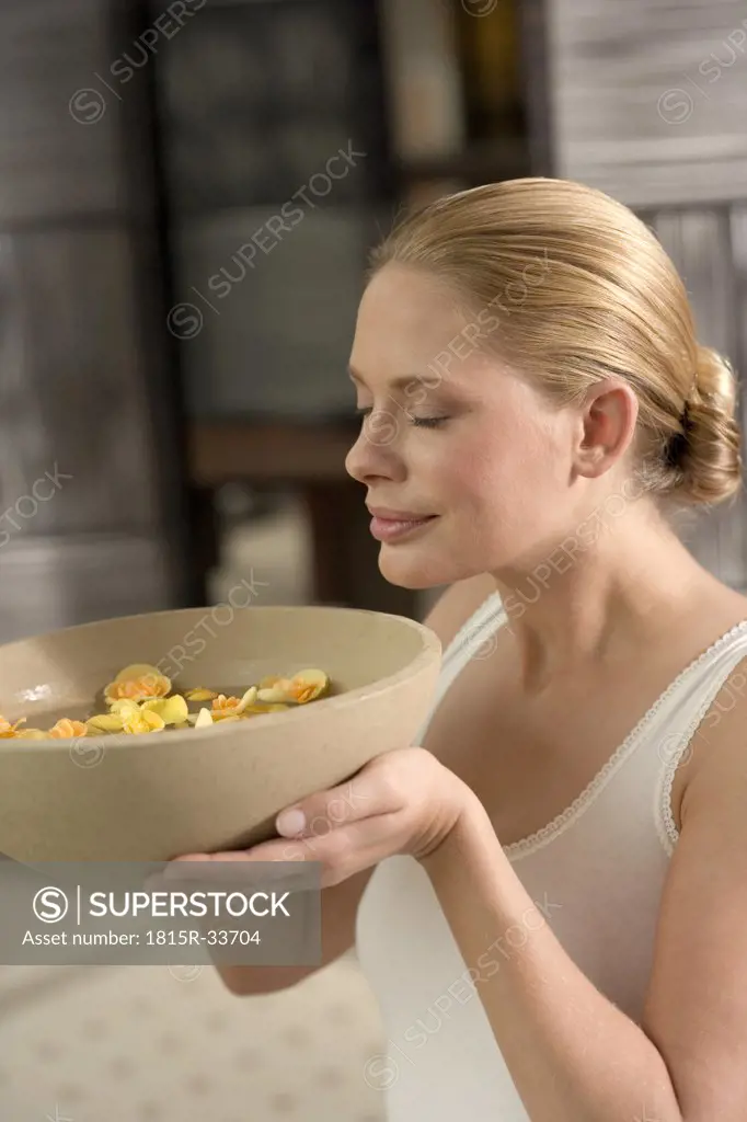 Germany, young woman holding bowl of flower petals, close-up