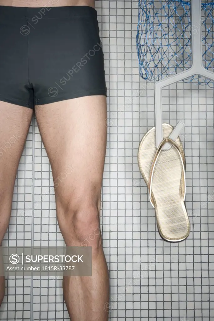 Man standing in changing room, holding hanger with flip-flops, low section