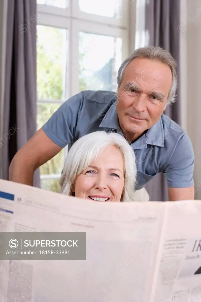 Senior Woman holding a newspaper, senior man behind, portrait