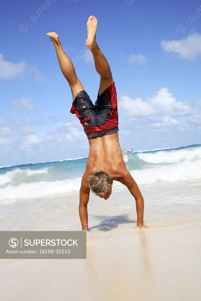 Young man making handstand on beach