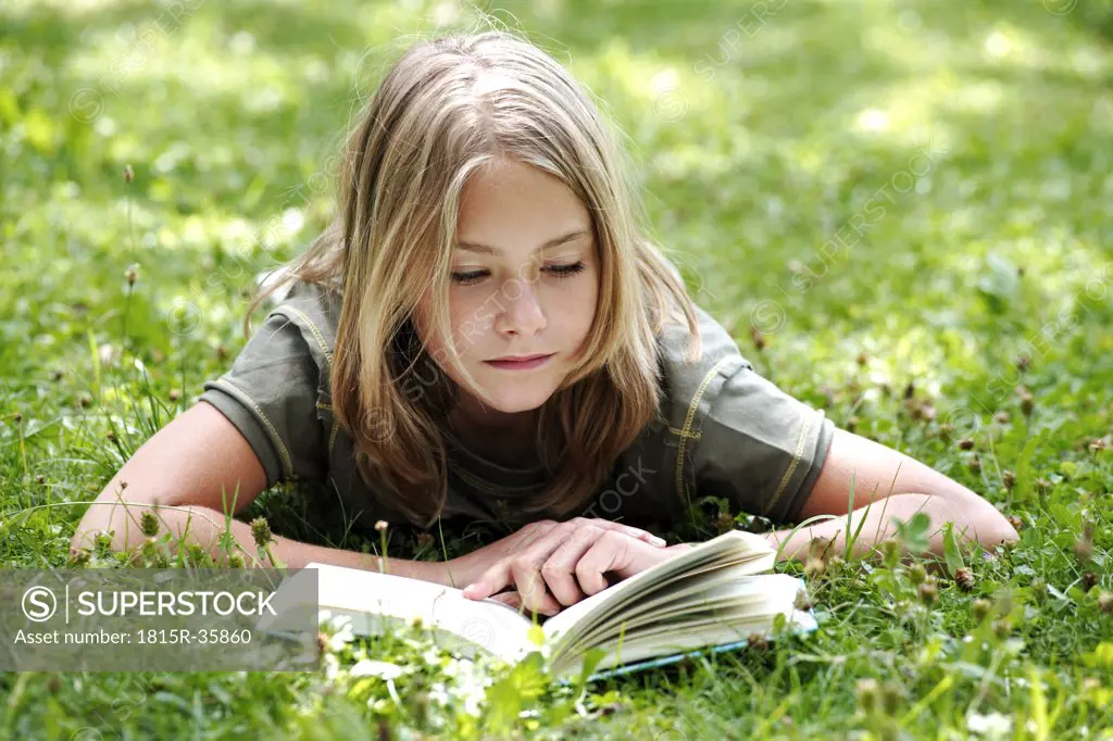 Girl (13-14) lying on grass reading, smiling