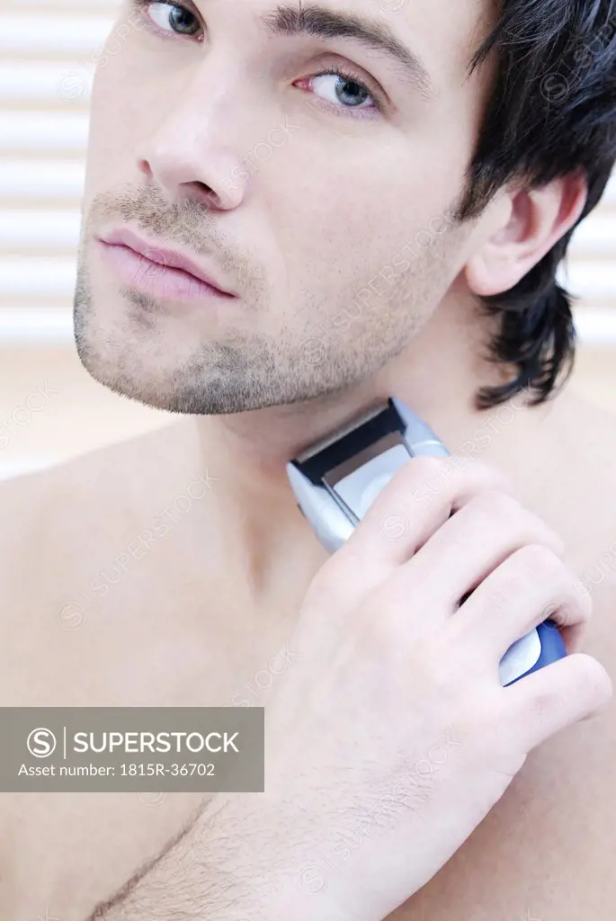 Young man using electric razor, portrait