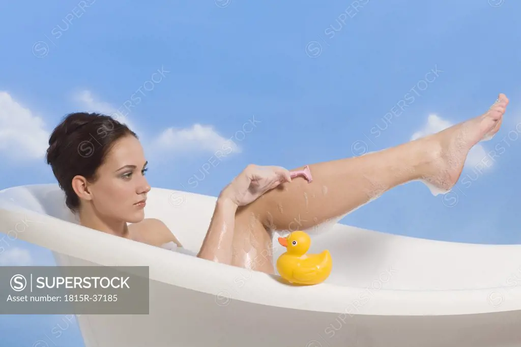 Young woman shaving legs in bath