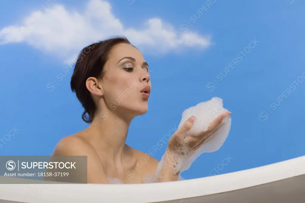 Young woman in bubble bath, blowing suds from hands, side view