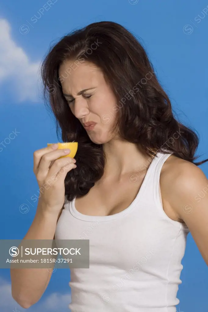 Young woman making a face, holding half of lemon, portrait