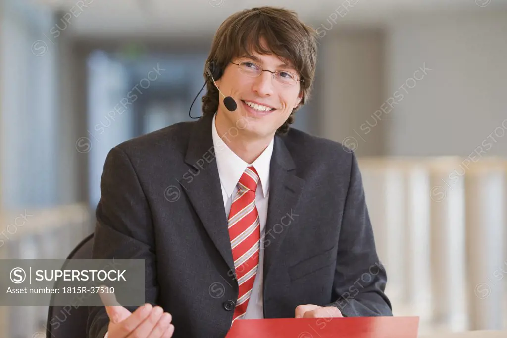 Young businessman wearing head set, smiling, portrait