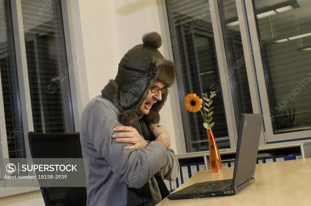 Man working at laptop, wearing cap, arms crossed
