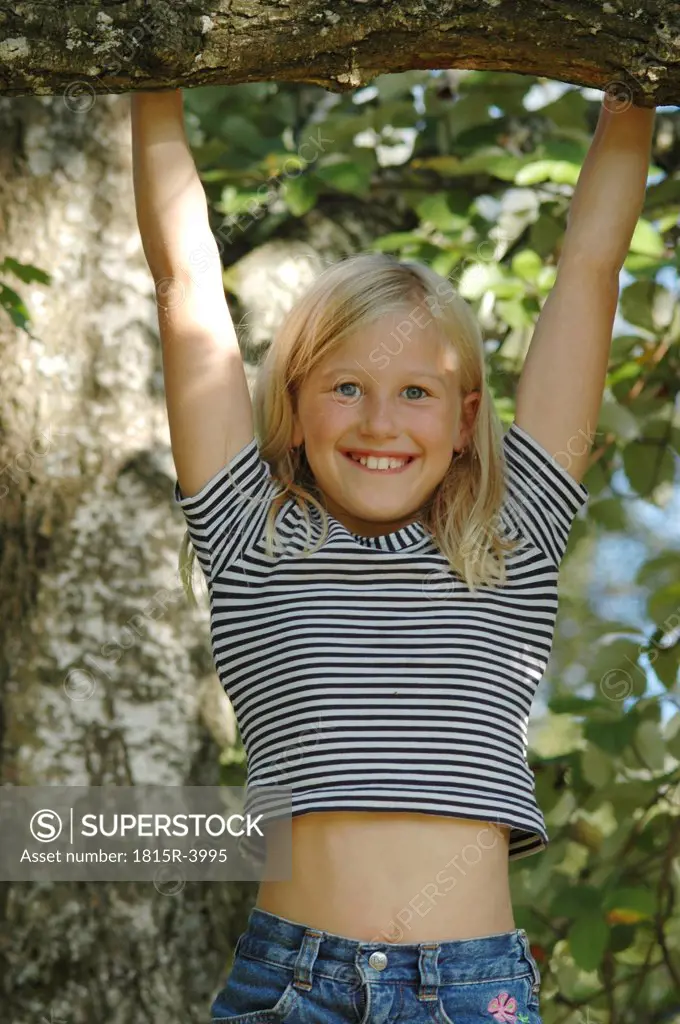 Girl (10-12) climbing on tree, smiling