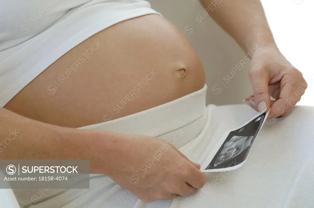 Expectant mother looking at sonogram of baby, mid section