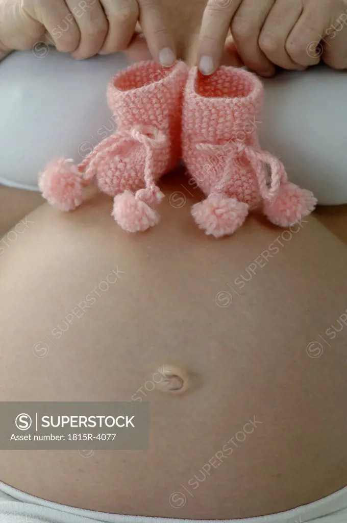Pregnant woman holding pair of baby shoes on belly, close-up, mid section