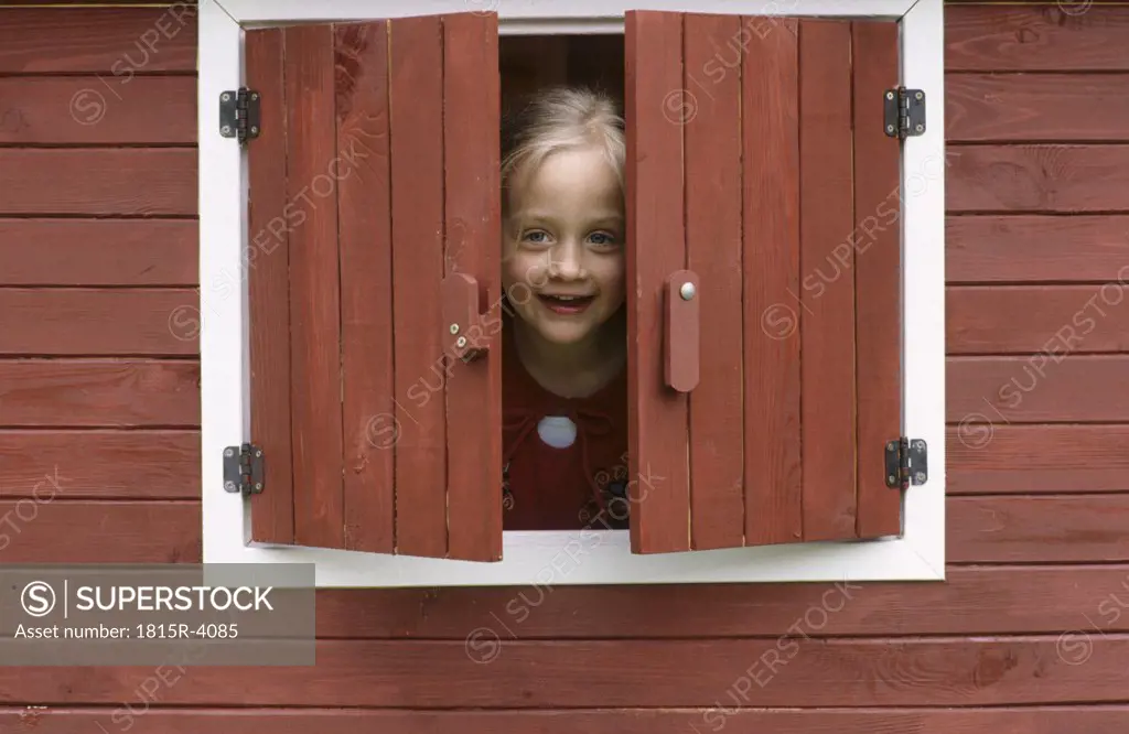 Girl (6-7) looking through window, smiling