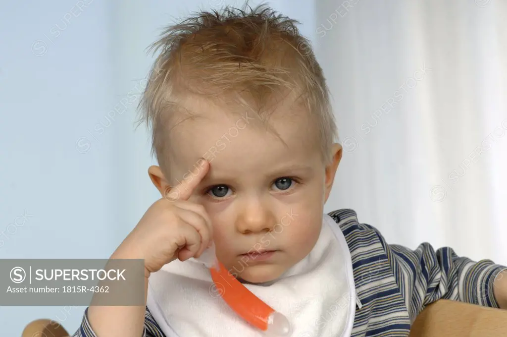 Boy (1-2) holding spoon, finger on forehead, portrait