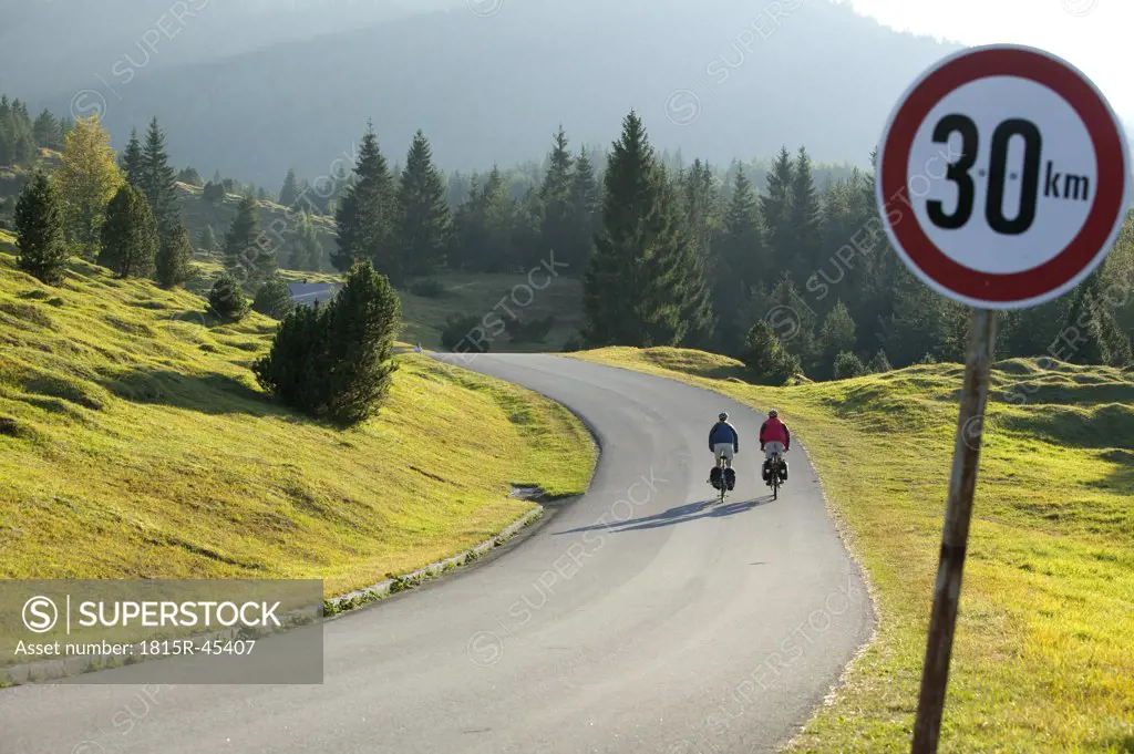 Germany, Bavaria, Mittenwald, Couple mountain biking, traffic sign in foreground
