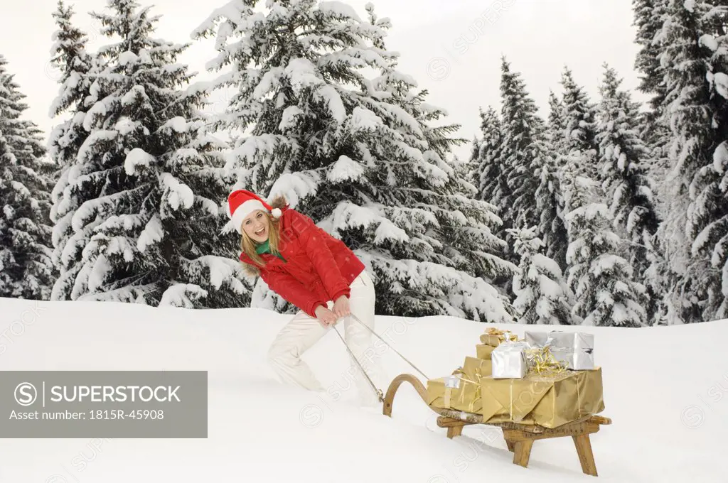 Austria, Salzburger Land, Altenmarkt, Young woman pulling sledge brimming with Christmas parcels